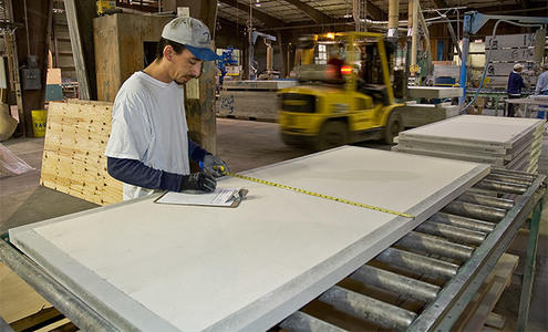 A man measuring a sheet of plywood in a factory for a product update.