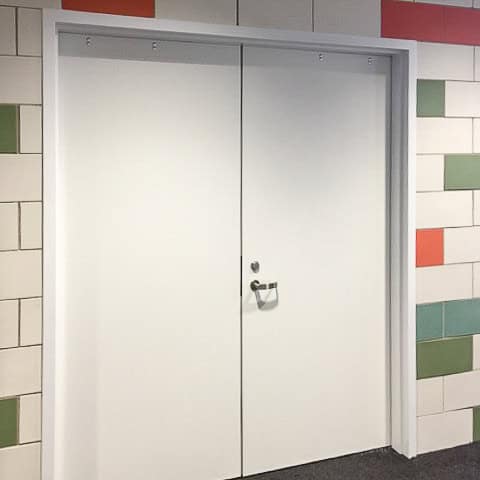 A closed double white Smooth Pultruded Fiberglass Door set in a wall with a multi-colored tile pattern. The door has a metal handle and visible hinges.