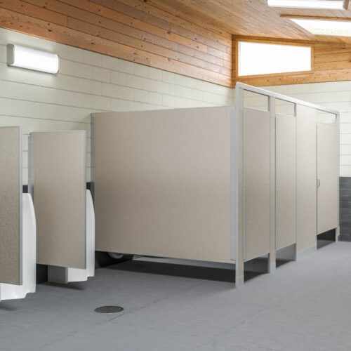 A clean, modern public restroom features two urinals on the left and three closed stalls with sleek commercial bathroom partitions on the right. The walls are light-colored, complemented by a wooden ceiling.