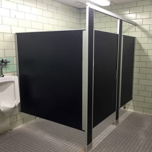 A public restroom featuring a urinal and two commercial bathroom partitions, surrounded by light green tiled walls and gray tiled flooring.