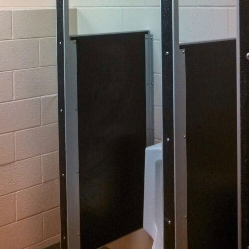 A partially enclosed urinal in a tiled bathroom with commercial bathroom partitions and metal dividers for privacy.