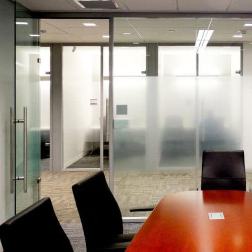 A modern office conference room with a wooden table, several black chairs, and LiteSpace glass walls featuring frosted sections for privacy and sleek aluminum framing.