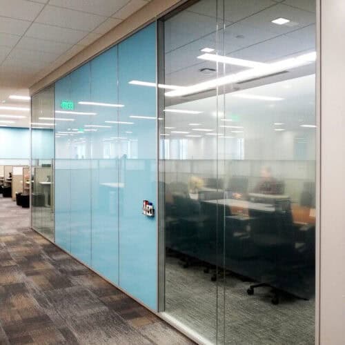 A modern office space with glass-walled conference rooms and cubicles featuring blue accents, neutral-toned carpets, and interior aluminum framing by LiteSpace.