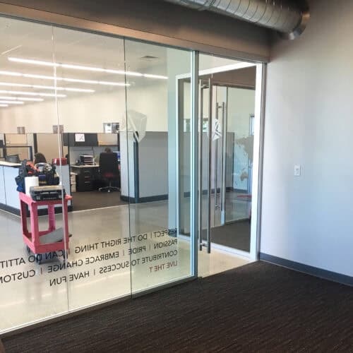 Glass office doors with motivational text lead to a modern LiteSpace workspace featuring cubicles and office equipment. The area, enhanced with aluminum framing, is well-lit and boasts a clean, professional appearance.