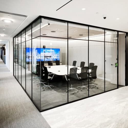 A modern conference room with aluminum framing and glass walls, featuring a large table, several office chairs, and a monitor displaying a cityscape image. This sleek interior is part of the LiteSpace corporate office setting.