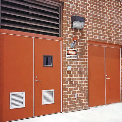 A brick building with three brown Pebble Grain Hybrid FRP Doors. A sign reading 