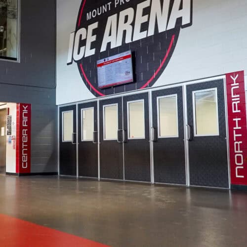 Entrance doors to an ice arena, featuring Pebble Grain Hybrid FRP Doors with the names 