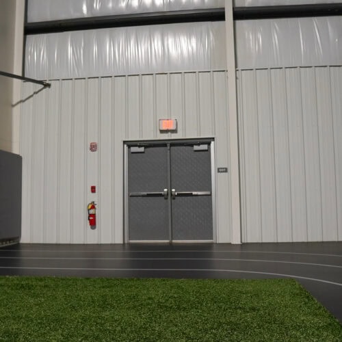 A double gray SL-17 door with an exit sign above it, situated on a pebble grain wall inside a building. A red fire extinguisher is mounted to the wall on the left side of the hybrid FRP door.