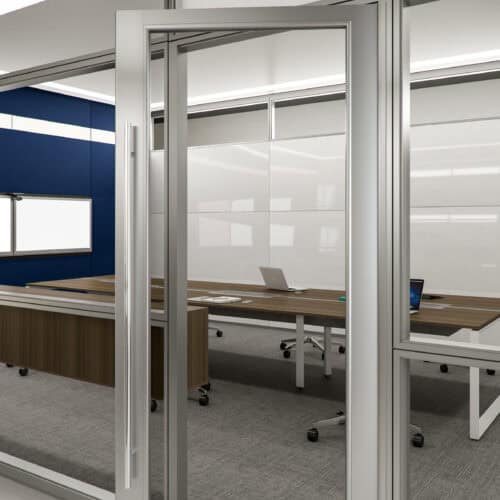 An open aluminum framed glass door reveals a modern conference room with two wooden tables, whiteboards, laptops, and office chairs on a carpeted floor.
