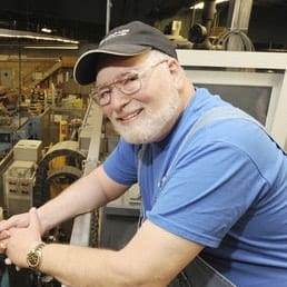 A man in a blue shirt is smiling at a machine in a factory.