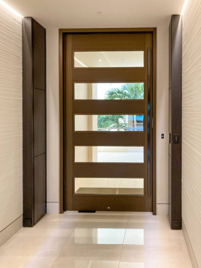 A modern entryway with wood grain door with rectangular window lite kits cut into it.