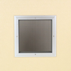 A square metal grille on a beige wall.