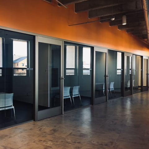 A hallway with several glass doors and chairs.