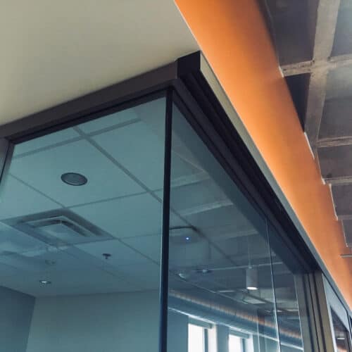 A glass wall in an office with an orange wall.