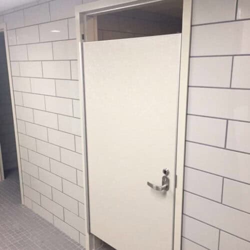 A hybrid FRP shower door between tiled walls in a restroom.