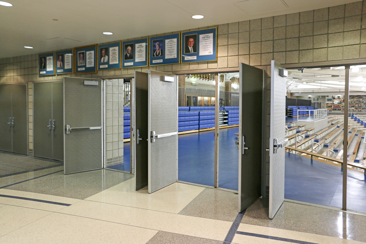 A hallway with a large number of doors that open to a school gymnasium.