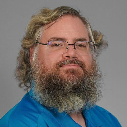 A man with a beard and glasses wearing a blue shirt. 