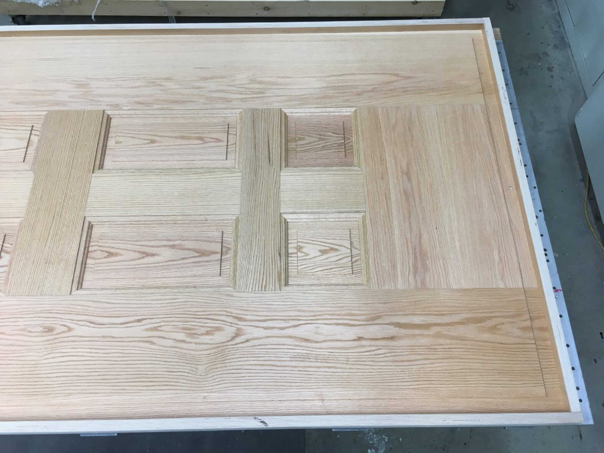 Unfinished rustic wood grain commercial door with a detailed panel design laid out on a workshop table.