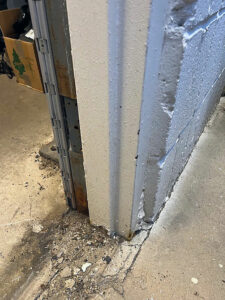 A close-up view of a deteriorating hollow metal door and frame with visible cracks accompanied by debris on the floor at a car wash.
