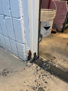 Base of a white painted hollow metal door and frame with visible deterioration at a car wash and debris on a concrete floor.