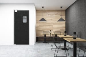 Minimalist cafe interior with wooden tables, black wire-frame chairs, concrete floor, and a black traffic door with a small window. Two pendant lights hang above each table set near a wood-paneled wall.