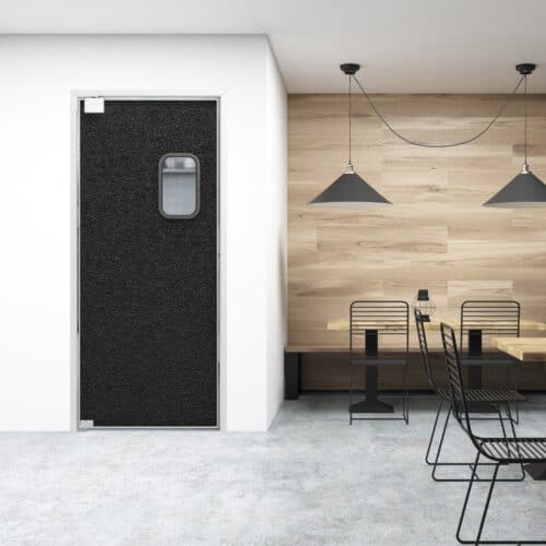 A modern room with black-framed tables and chairs, two pendant lights, a wooden accent wall, and a black traffic door with a small window.