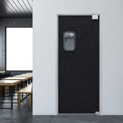 A black traffic door with a small window is set within a white wall. The room features wooden tables and chairs, with a large window providing natural light.