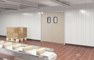 A clean, industrial room with red floor tiles, stainless steel equipment, a pallet with boxes, and double doors with small windows.