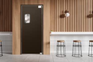 A cafe interior with wooden slatted walls, white countertops, four wooden stools, and a black door with a small window.