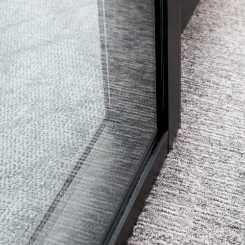 A close-up view of a glass door next to a grey carpeted floor, with the light reflecting off the glass. The design subtly incorporates glass partition walls with enhanced privacy.