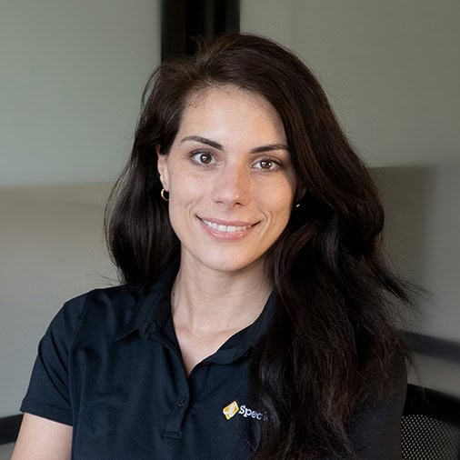 A person from our team with long dark hair, wearing a black polo shirt, is smiling while seated indoors.