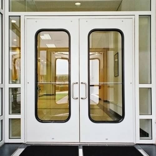 Smooth aluminum flush doors with metal handles welcome you, featuring large oval windows nestled within a sleek, modern building facade.