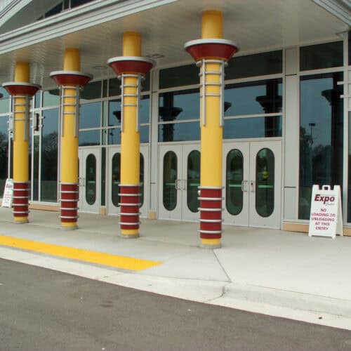 Yellow pillars and aluminum doors adorn the entrance of the expo building. A sign reads 