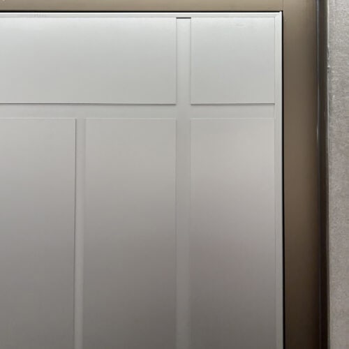 Close-up of a smooth aluminum panel with rectangular indentations and a metallic frame, reminiscent of a flush door design, on the right edge.