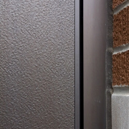 Close-up of an embossed aluminum panel next to a brick wall, with a narrow black gap between them resembling the sleek alignment of flush doors.