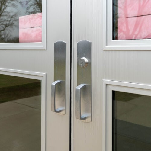 A pair of sleek, fluted aluminum flush doors features sturdy metal handles and a central keyhole lock. Inside, pink papers are neatly taped to the glass panels.