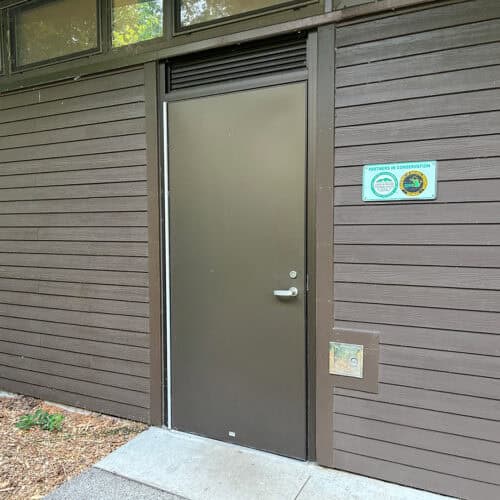 A closed brown fluted aluminum flush door on a wooden building features a 