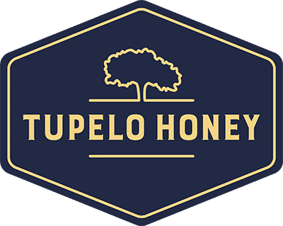 The Tupelo Honey logo features a tree silhouette above the text, enclosed in a hexagonal border reminiscent of elegant restaurant doors. It boasts a navy background with tan lettering that adds a touch of sophistication.
