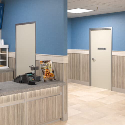 A clean, modern fast food restaurant interior features a counter, cash register, promotional food sign, and a restroom door equipped with a FlexFit™ Field-Adjustable Interior Aluminum Door Frame in the background.