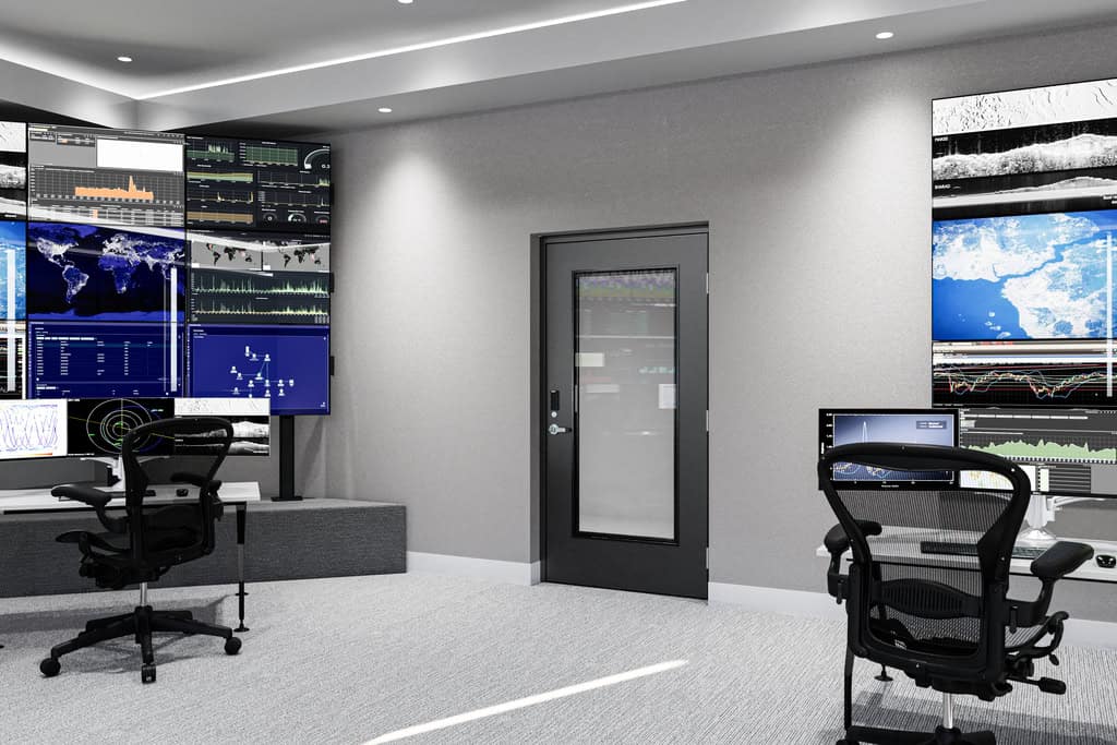 A modern control room with large display screens showing maps, data, and graphs, two empty office chairs, and a national account commercial door solution in the center of the back wall.