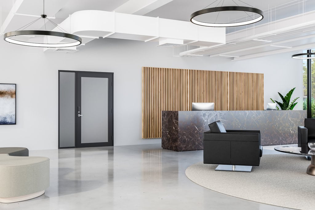 Modern office lobby with a marble reception desk, wood panel accent wall, black seating, circular light fixtures, large windows providing natural light, and secure entryways enhanced by national account commercial door solutions.