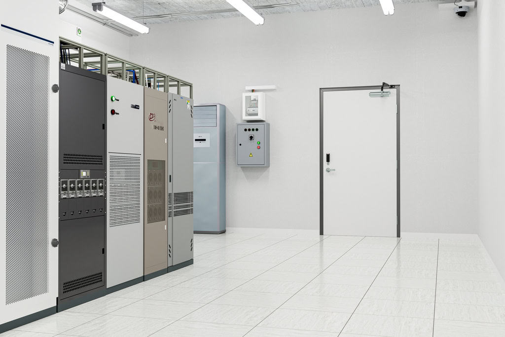 A clean, white server room with several server racks, electrical panels, tiled floors, and fluorescent ceiling lights—secured by national account commercial door solutions for optimal safety.