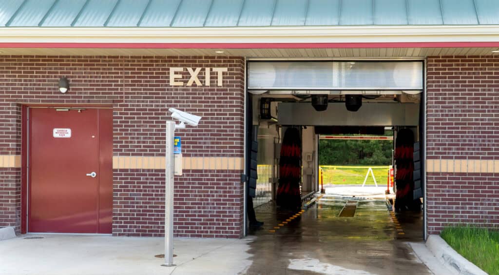 Brick building with a red door and an "EXIT" sign above the opening of an automated car wash, viewed from outside, reminiscent of modern healthcare solutions in its efficient, streamlined design.