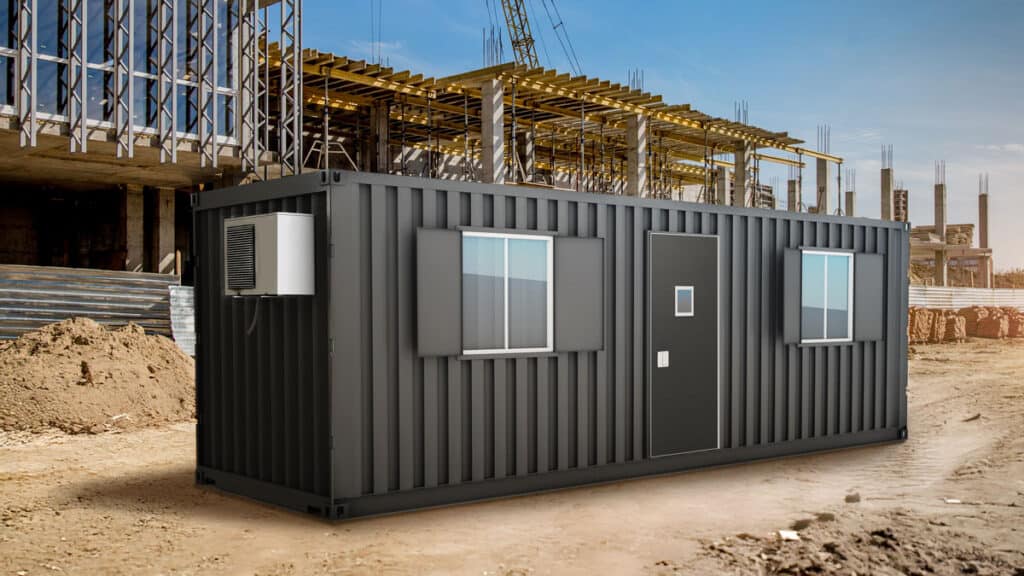 A black shipping container converted into an office with windows and a national account commercial door solution, placed at a construction site with building structures in the background.