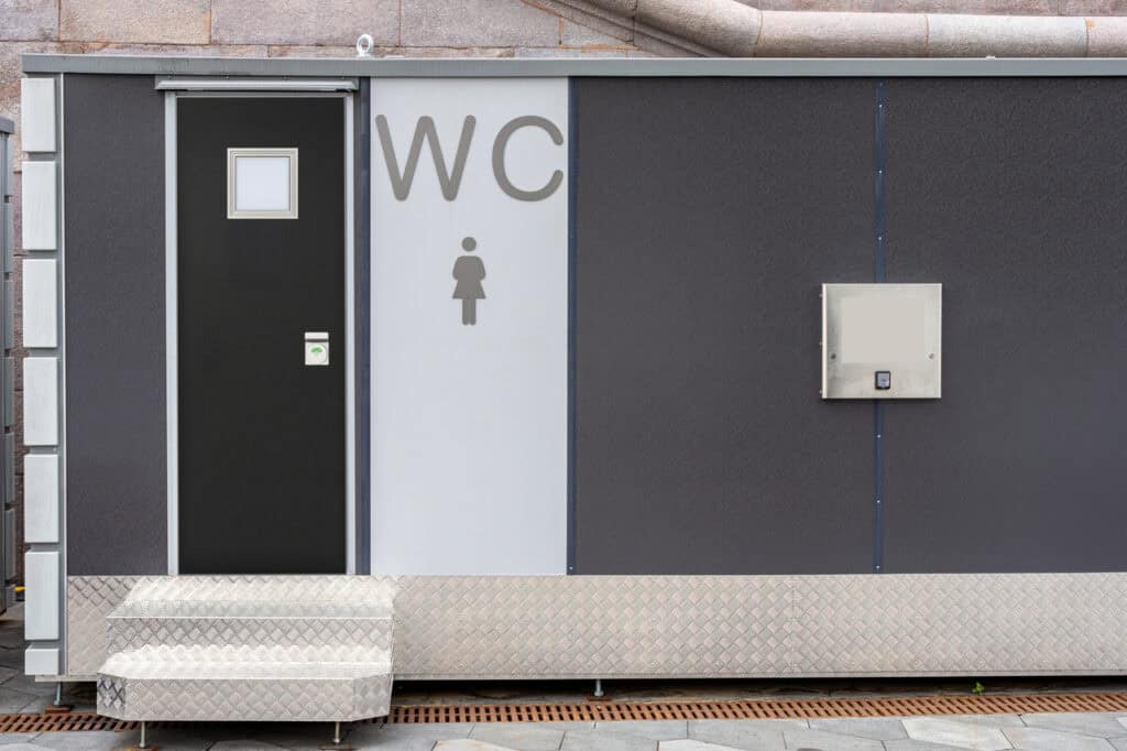 A public restroom with a black door, a “WC” sign and female symbol, plus metal steps leading up—ideal for OEM Account Solutions for Modular and Prefabricated Mobile Facilities.