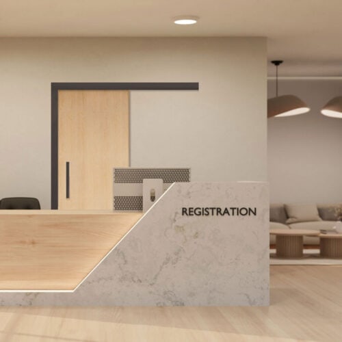 Modern registration desk with a light wood and marble design, complemented by sleek wood veneer doors, a computer monitor, and a waiting area with chairs in the background.